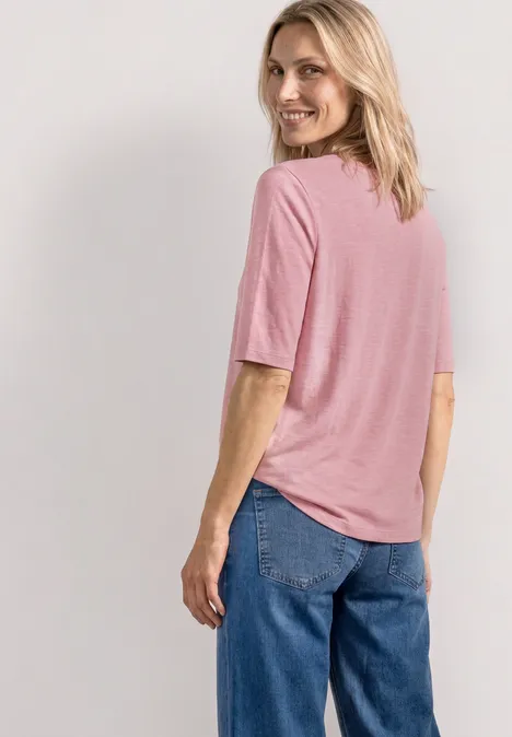 Eine Person steht mit dem Rücken zur Kamera, trägt ein rosafarbenes T-Shirt und blaue Jeans.