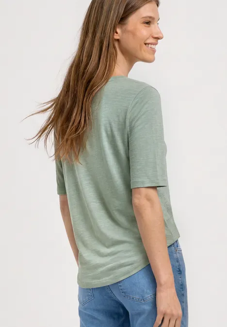 Basic Shirt met ronde hals in Unifarbe eucalyptus green Een vrouw van achteren draagt een lichtgroen shirt en een blauwe spijkerbroek.