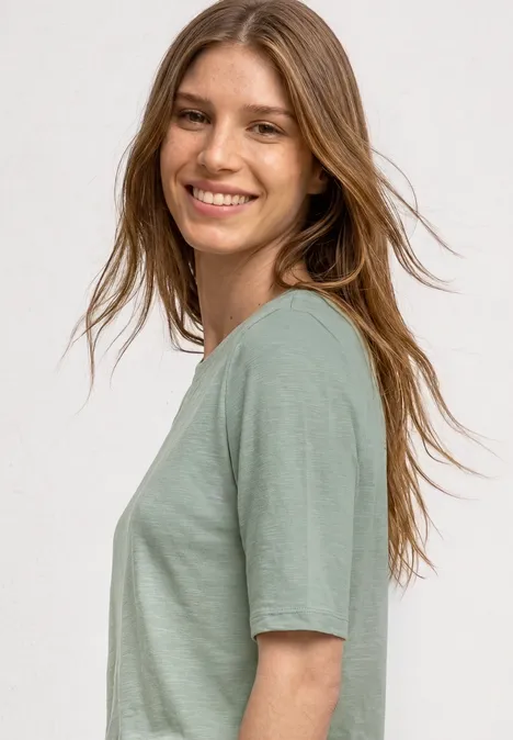 Basic Shirt met ronde hals in Unifarbe eucalyptus green Iemand in profiel draagt een lichtgroen T-shirt tegen een neutrale achtergrond.