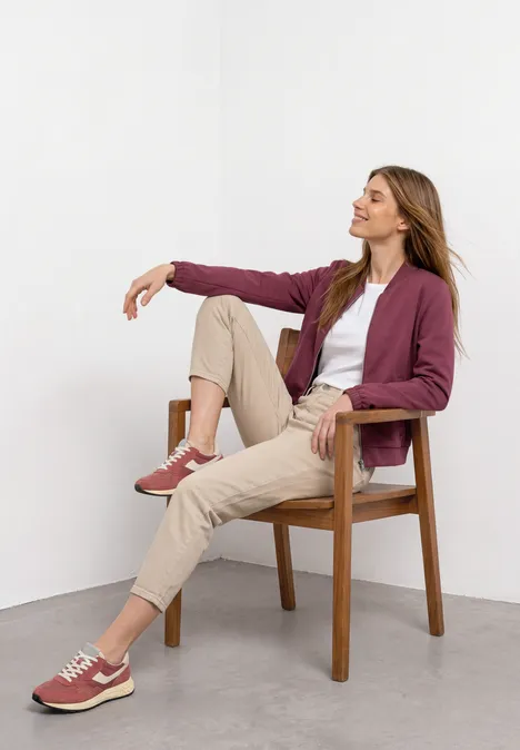 Une femme détendue assise sur une chaise en bois, vêtue de tenues décontractées, regardant sur le côté.