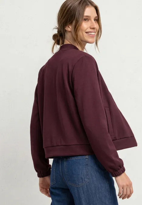 Eine Frau in weinrotem Blouson und blauen Jeans blickt lächelnd über die Schulter.