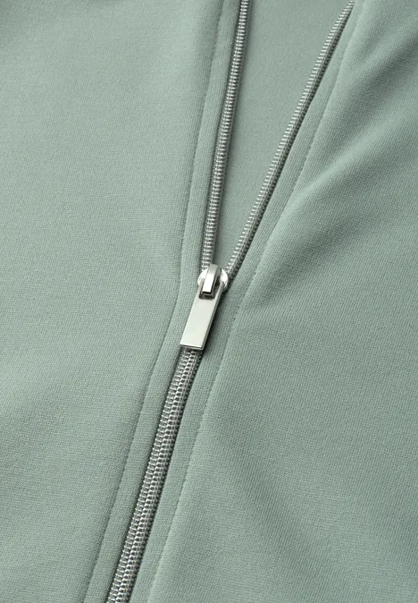 Nahaufnahme eines salbeigrünen Kleidungsstücks mit einem silbernen Reißverschluss.