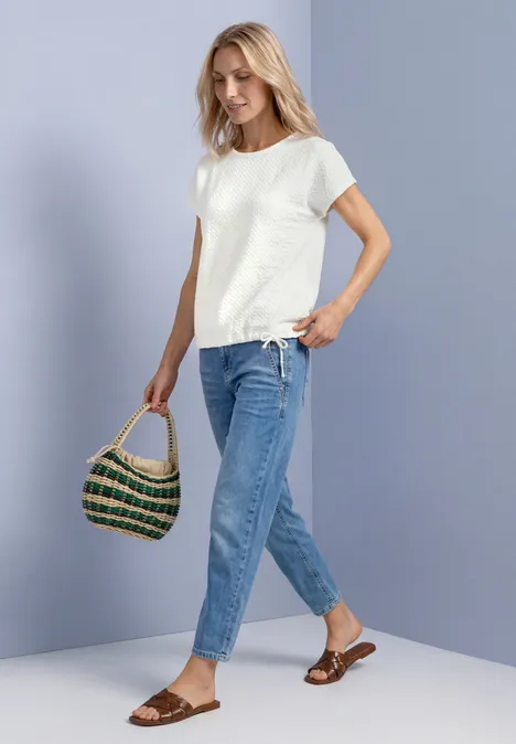 T-Shirt aus Spitze mit Rundhals off white Frau in weißem T-Shirt, blauen Jeans und Sandalen hält eine geflochtene Tasche und geht.