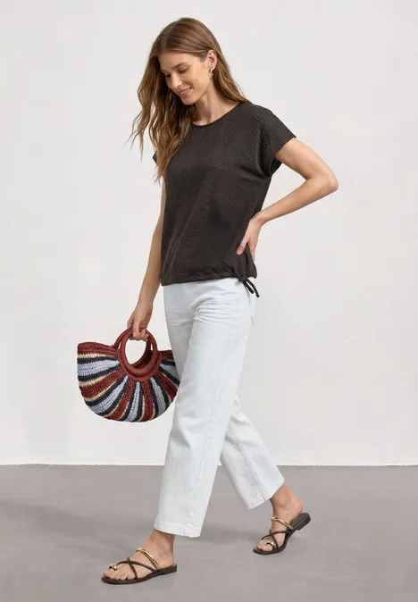 T-Shirt aus Spitze mit Rundhals black coffee Eine Frau trägt weiße Hosen, schwarzes T-Shirt und Sandalen und hält eine bunte, rund gestreifte Handtasche.