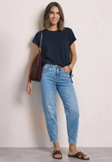T-Shirt aus Spitze mit Rundhals darkest blue Frau vor hellem Hintergrund in dunkelblauem T-Shirt, Jeans, braunen Sandalen und Schultertasche, sie lächelt.