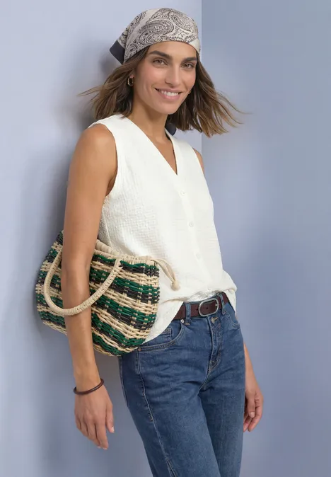 Top met V-hals en decoratieve knoopsluiting off white Vrouw met wit topje, spijkerbroek en hoofddoek, glimlachend met een gevlochten strooien tas.