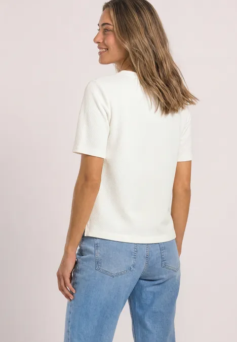 T-shirt à col rond et texturé off white Frau von hinten in weißem Kurzarmshirt und Jeans, sie lächelt und blickt seitlich, mittelblonde Haare.
