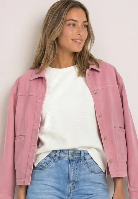 T-shirt à col rond et texturé off white Frau in blauer Jeans, weißem Pullover und pinker Jacke, die lächelnd seitlich posiert.