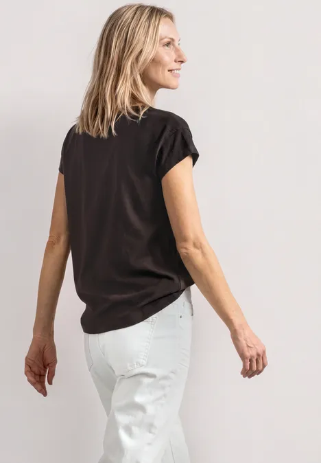 T-Shirt mit Rundhals und Foliendetails black coffee Frau von hinten in schwarzem T-Shirt und weißer Hose vor hellem Hintergrund.
