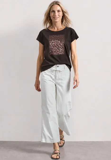 T-Shirt mit Rundhals und Foliendetails black coffee Frau in schwarzem T-Shirt mit Leoparden-Print, weiten weißen 7/8-Jeans und schlichten Sandalen steht lässig da.