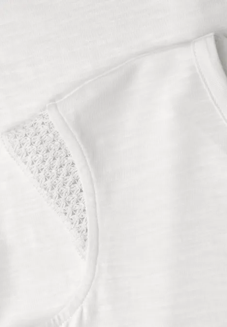 Nahaufnahme eines weißen T-Shirts mit zarter Spitze am Ärmel und feiner Struktur.