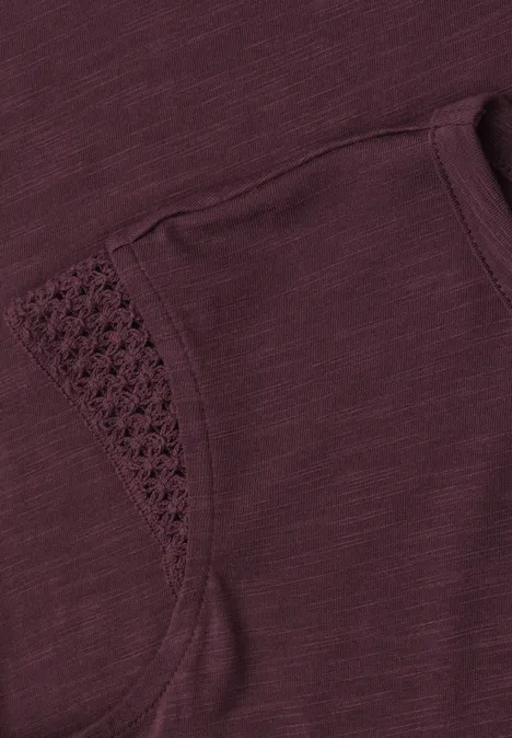 Nahaufnahme eines dunkelvioletten Shirts mit Tasche und filigraner Häkelbordüre.