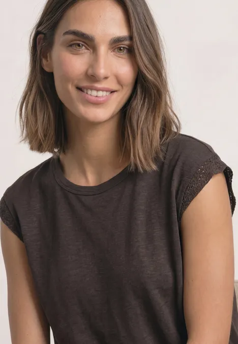 Porträt einer lächelnden jungen Frau mit braunen Haaren und dunkelbraunem T-Shirt vor hellem Hintergrund.