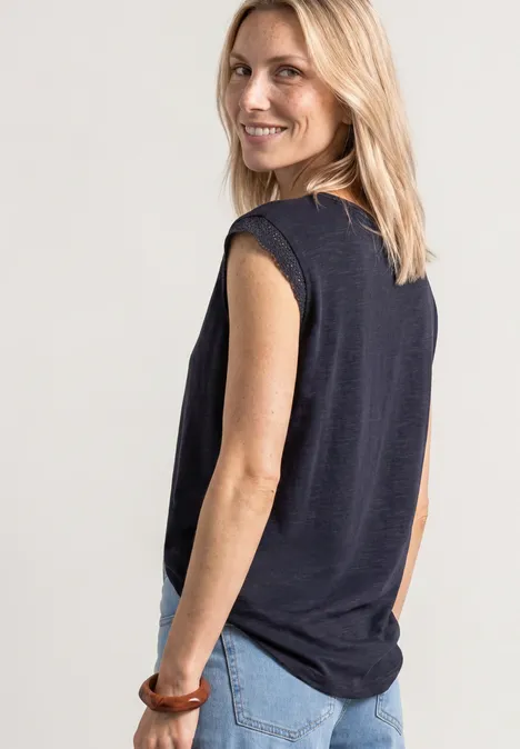 Eine Frau von hinten in einem schwarzen ärmellosen Top und blauen Jeans, blondes Haar und Holzarmreif am Handgelenk.