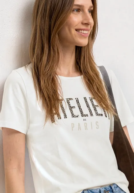 Frau trägt weißes T-Shirt mit Schriftzug 'BELIEVE PARIS' und Schultertasche.