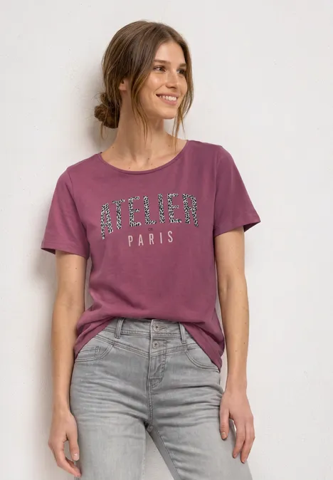 T-Shirt mit Rundhals und Frontprint dark clouded blush Frau trägt pinkes 'Atelier Paris'-T-Shirt und graue Jeans vor neutralem Hintergrund.
