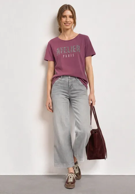 T-Shirt mit Rundhals und Frontprint dark clouded blush Frau in lässigem Outfit: violettes T-Shirt, weite Jeans, Sneaker und burgunderrote Tasche.