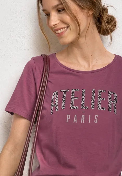 T-Shirt mit Rundhals und Frontprint dark clouded blush Lächelnde Frau in weinrotem T-Shirt mit 'ATELIER PARIS'-Schriftzug, seitlicher Dutt, vor heller Wand.