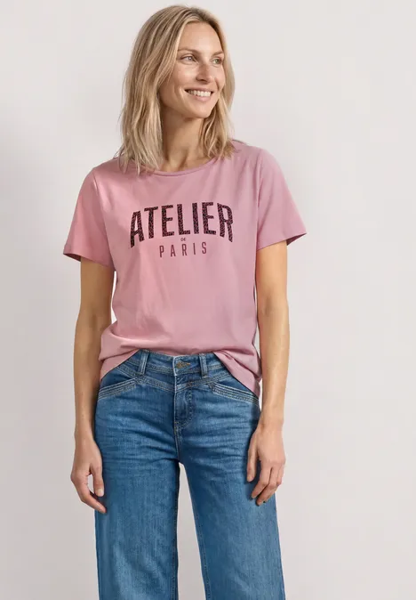 T-Shirt mit Rundhals und Frontprint vintage blush Person trägt rosa T-Shirt mit Aufschrift 'ATELIER PARIS' und blaue Jeans.