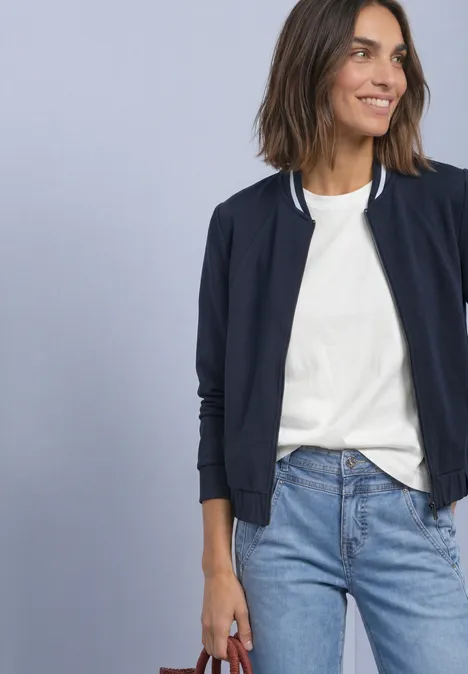 Langarm Jacke im Silk-Look mit Zipper darkest blue Eine Frau trägt weißes T-Shirt, blaue Jacke und Jeans, hält eine rote Handtasche vor hellblauem Hintergrund.