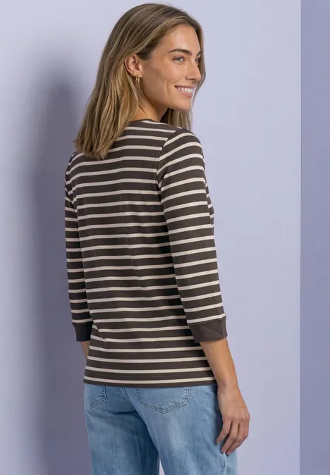 Frau im gestreiften 3/4-Arm-Shirt und Jeans, dreht den Rücken mit Blick über die Schulter vor hellem Hintergrund