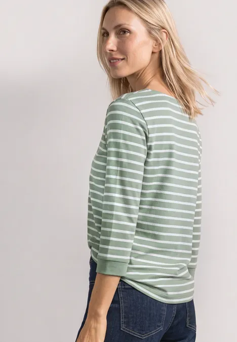 Eine Frau im grünen, weiß gestreiften Langarmshirt blickt über die Schulter.