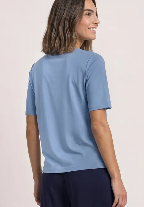 Shirt met ronde hals en contrasterende details northern blue Vrouw in lichtblauw T-shirt en donkere broek, glimlachend zijwaarts voor lichte achtergrond.