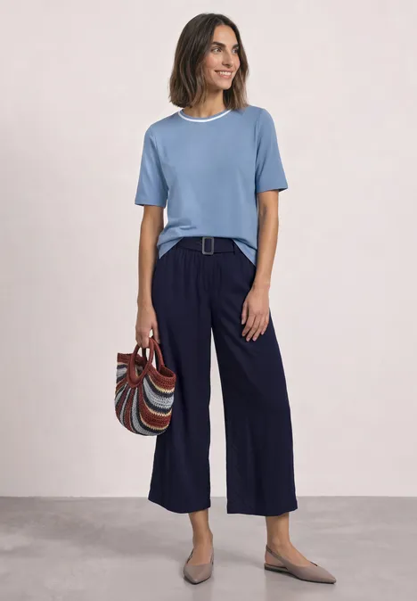 Shirt met ronde hals en contrasterende details northern blue Vrouw met blauwe t-shirt en losse donkerblauwe broek, met gestreepte tas en platte schoenen, glimlachend.