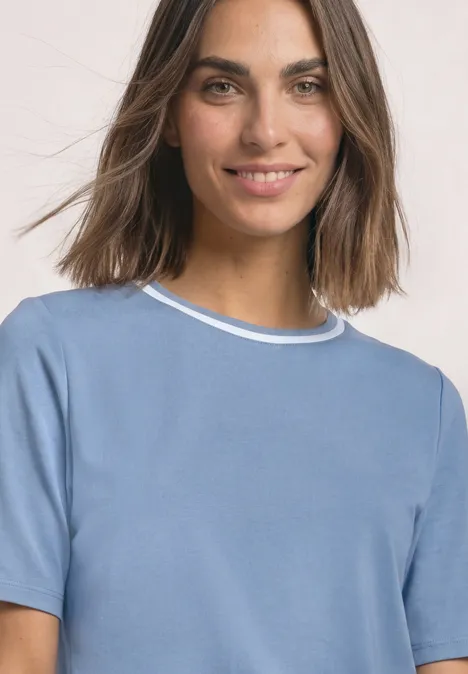 Shirt met ronde hals en contrasterende details northern blue Een glimlachende vrouw met bruin haar draagt een lichtblauw shirt voor een lichte achtergrond.