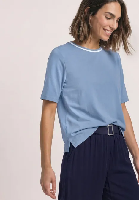 Shirt met ronde hals en contrasterende details northern blue Een glimlachende vrouw in een lichtblauw T-shirt met witte kraag en wijde donkerblauwe broek met riem.