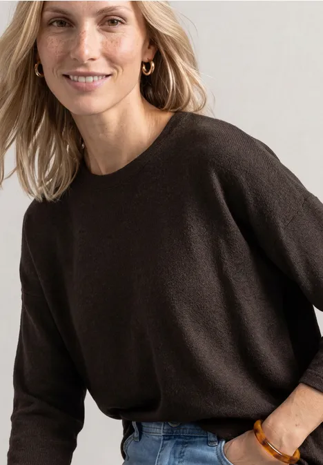 Frau in schwarzem Pullover und Jeans lächelt entspannt in die Kamera.