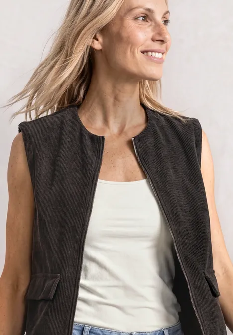 Vest met ronde hals in corduroy-look black coffee Vrouw met licht haar draagt een donkerbruine suède bodywarmer op een wit topje, lacht schuin.