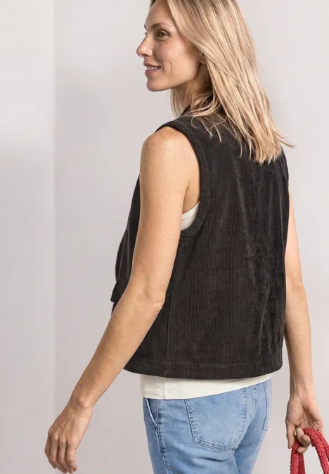 Vest met ronde hals in corduroy-look black coffee Vrouw in zijaanzicht met zwart vest, wit topje en jeans, houdt een rode tas vast.