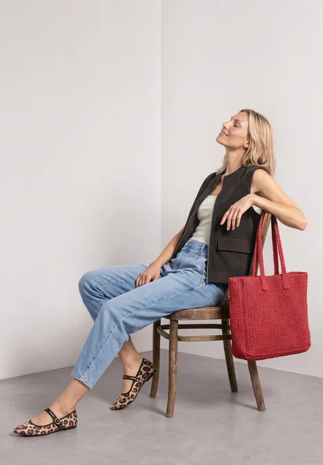 Vest met ronde hals in corduroy-look black coffee Vrouw zit ontspannen op een stoel voor een witte muur, draagt jeans, vest, sandalen en grote rode tas.