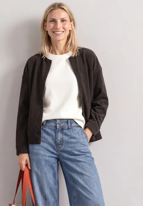 Femme souriante en t-shirt blanc, veste noire, jean bleu et sac orange.