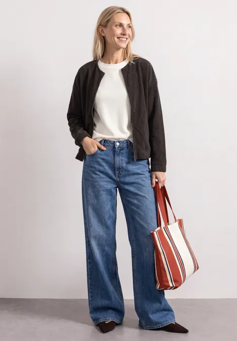 Femme en veste noire, t-shirt blanc, jean large et sac rayé.