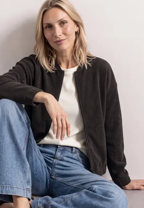 Une femme décontractée assise en veste noire, top blanc et jean bleu.