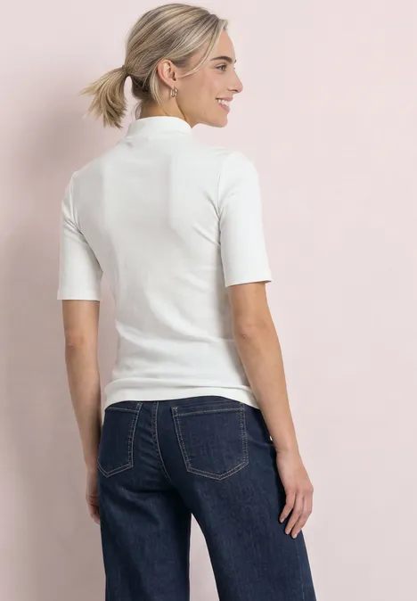 Shirt met col in ribbelpatroon off white Vrouw van achteren met wit shirt met korte mouwen en blauwe spijkerbroek voor een roze achtergrond.