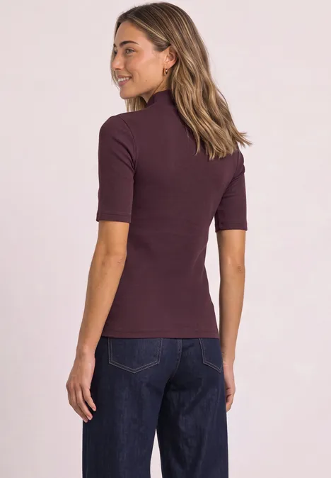 Shirt met col in geribbelde structuur rustic rouge Frau von hinten, trägt ein bordeauxfarbenes Kurzarmshirt und dunkle Jeans.