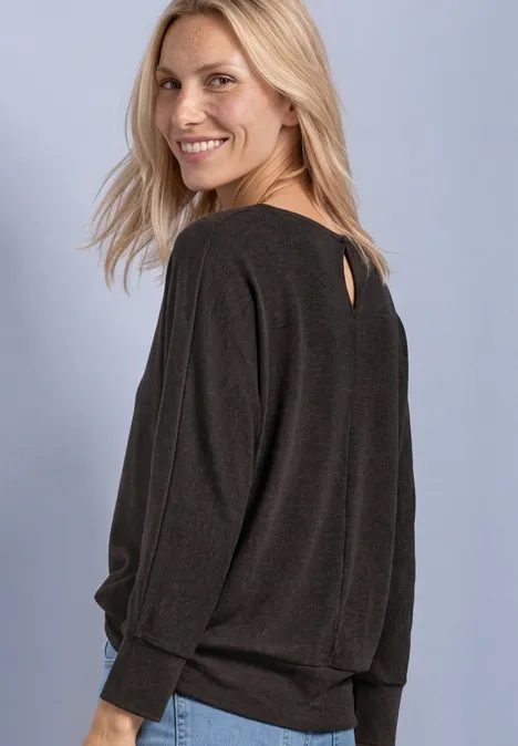 Eine blonde Frau lächelt, trägt einen lockeren dunklen Pullover und blickt seitlich über die Schulter.