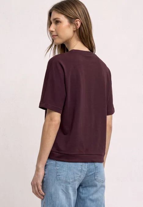 T-Shirt mit Rundhals im Silk-Look rustic rouge Junge Frau in weinrotem T-Shirt und hellblauen Jeans, in Rück- und Seitenansicht vor hellem Hintergrund.