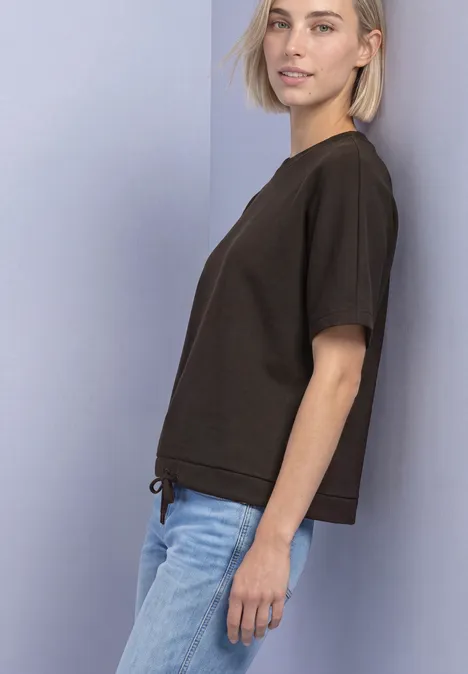T-Shirt mit Rundhals im Silk-Look black coffee Junge Frau im braunen T-Shirt und blauen Jeans steht seitlich vor heller Wand.