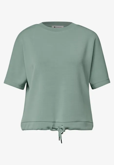 Salbeigrünes, locker geschnittenes Kurzarmshirt mit Rundhalsausschnitt und Kordelzug am Taillenbund.