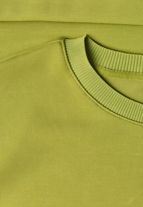 Pull vert clair à col rond, gros plan sur le col et l'épaule.