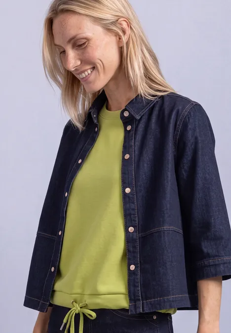 Femme blonde en veste en jean et tee-shirt vert, souriante, regard sur le côté