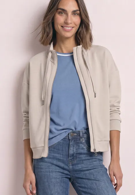 Jacke im Silk-Look mit Rippdetails clay sand Frau trägt beige Jacke, blaues T-Shirt und Jeans, lächelt vor hellem Hintergrund.