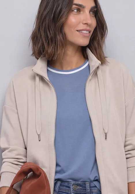 Jacke im Silk-Look mit Rippdetails clay sand Frau trägt beigen Cardigan über blauem Shirt und hält eine braune Tasche.