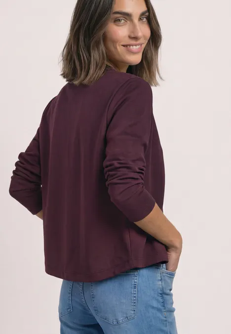 Strick-Look Jacke mit dekorativen Knöpfen rustic rouge Frau in bordeauxrotem Langarmshirt und Jeans, von hinten, mit Blick über die Schulter.