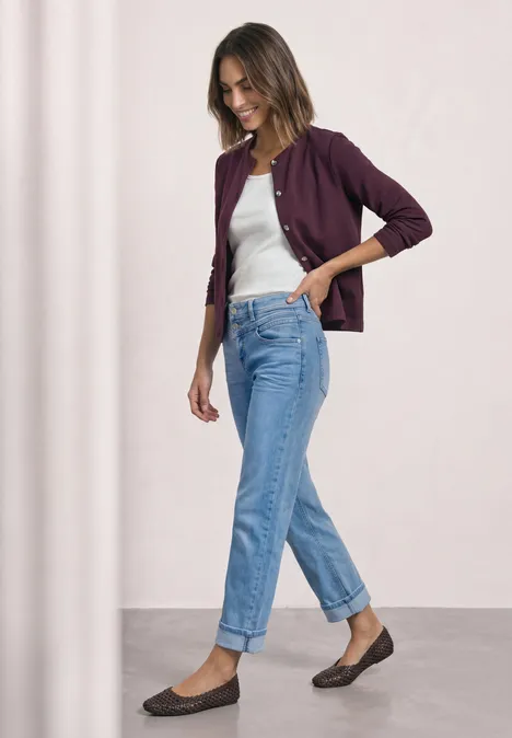Strick-Look Jacke mit dekorativen Knöpfen rustic rouge Frau in Jeans, weißem Top und lila Cardigan steht seitlich und lächelt.