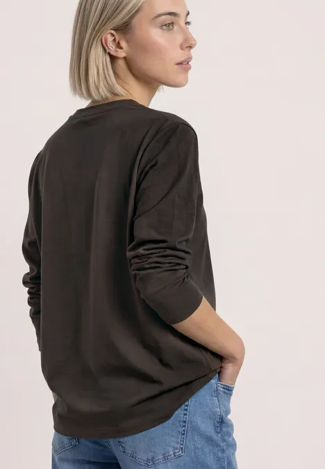 Strick-Look Jacke mit dekorativen Knöpfen black coffee Eine Frau in braunem Langarmshirt und blauen Jeans steht seitlich abgewandt vor hellem Hintergrund.